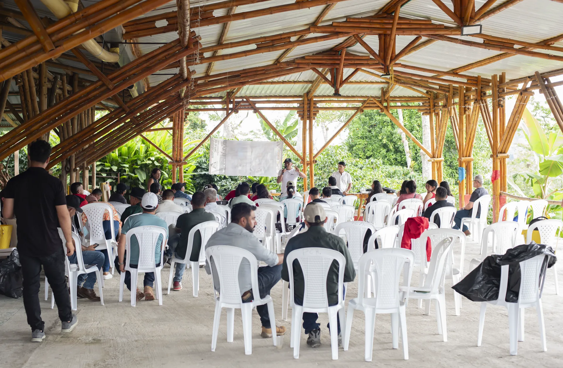 Personas reunidas en un salón campestre con sillas bajo una estructura de madera